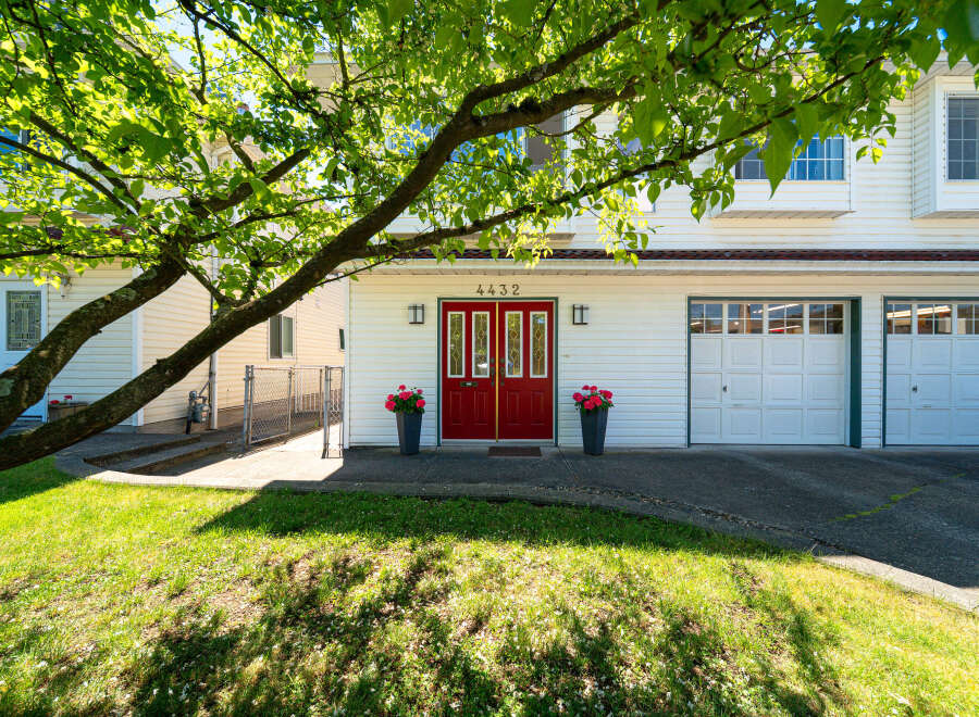 Charming home featuring a bright red double door entrance, flanked by two large planters filled with vibrant pink flowers.