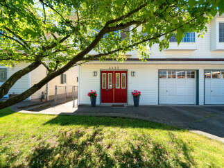 Charming home featuring a bright red double door entrance, flanked by two large planters filled with vibrant pink flowers.