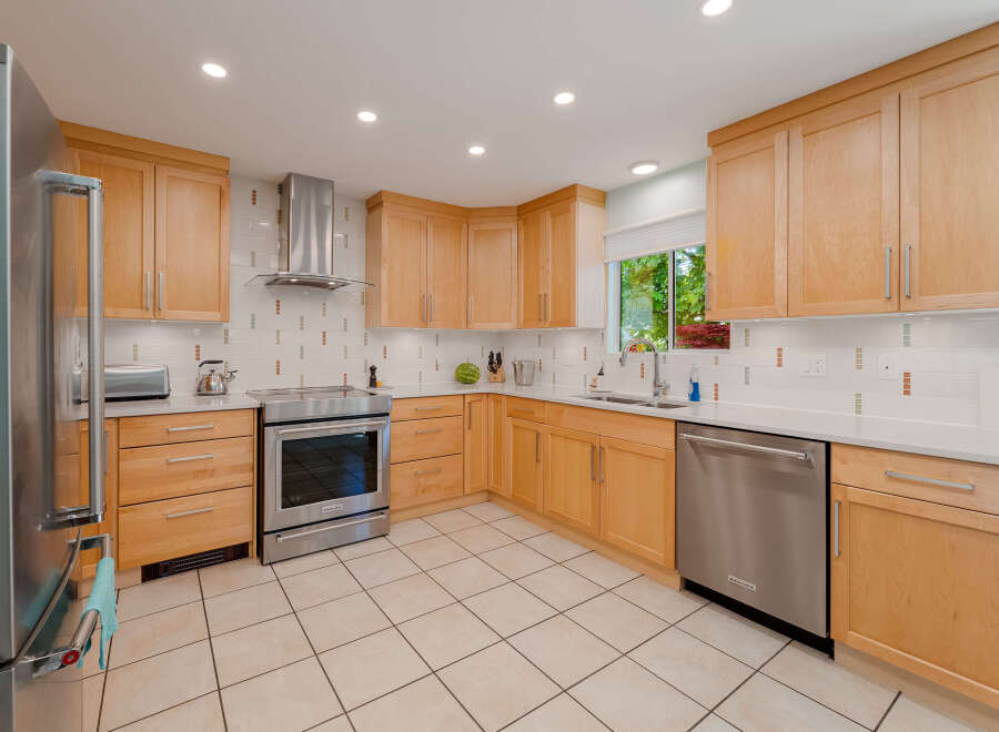 This spacious kitchen features light wood cabinetry and sleek stainless steel appliances, including a modern range and dishwasher.
