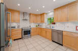 This spacious kitchen features light wood cabinetry and sleek stainless steel appliances, including a modern range and dishwasher.