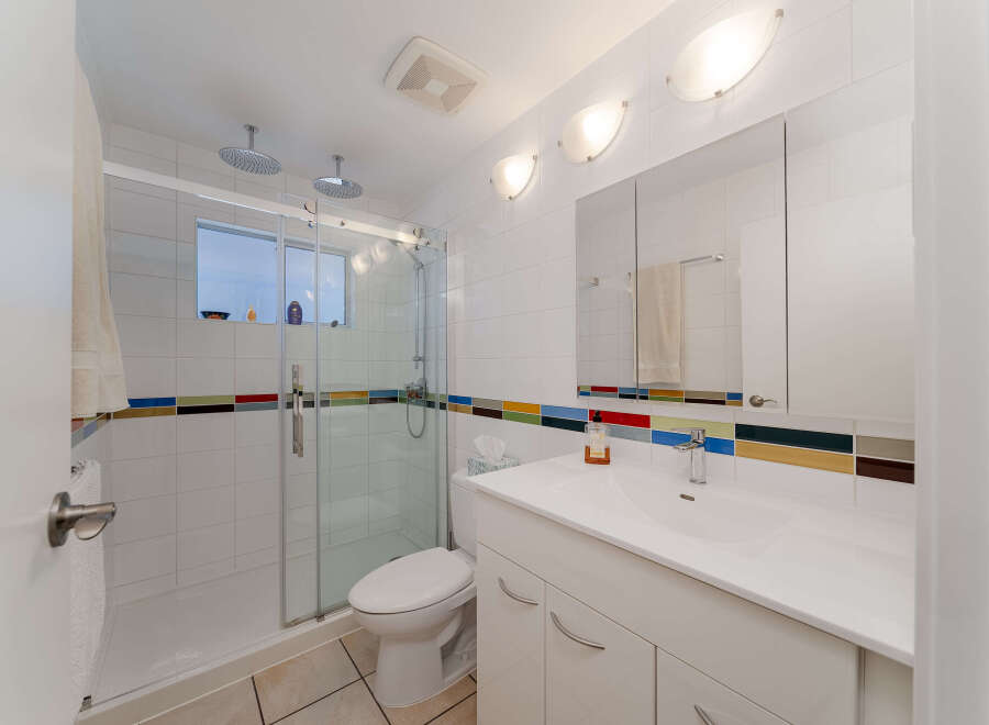 Experience modern comfort in this beautifully appointed bathroom, featuring a spacious glass-enclosed shower with dual showerheads and a sleek vanity with a large mirror.