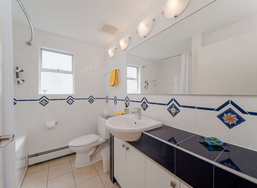 This bright and clean bathroom features a white tiled shower with a curved rod and a white shower curtain.