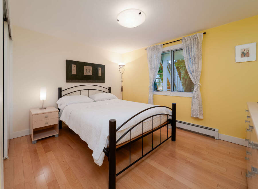 Bright and inviting bedroom featuring a comfortable queen-size bed with crisp white linens, complemented by a sleek black metal frame.