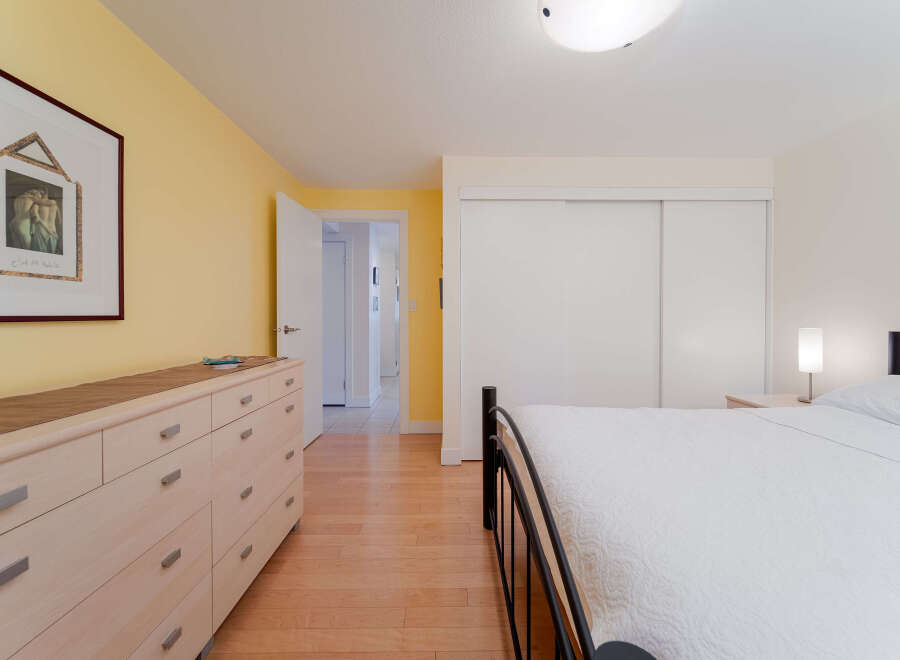 This bright bedroom features a large dresser with ample storage and a framed piece of art on a cheerful yellow accent wall.