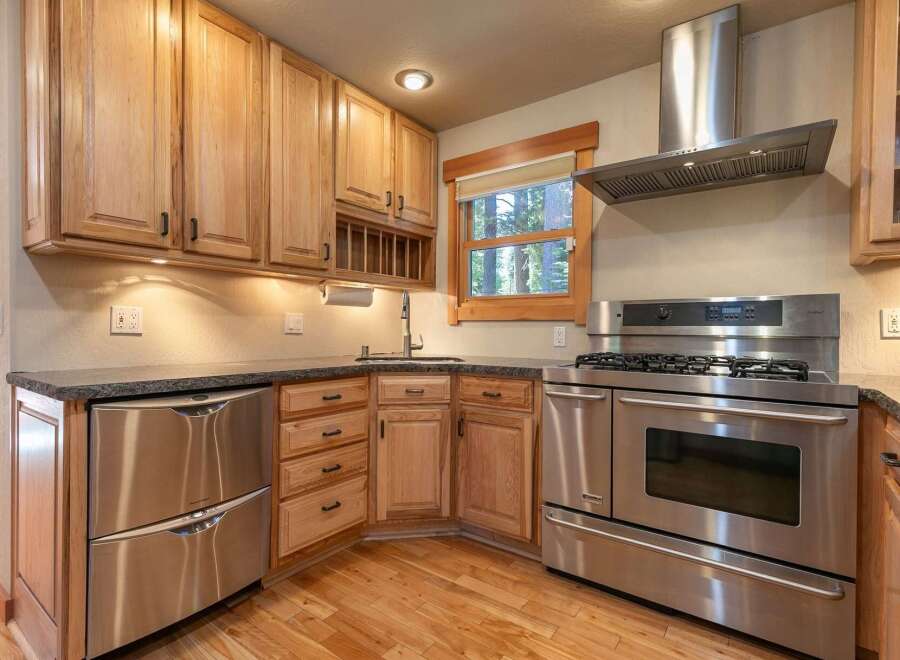 This charming kitchen features beautiful light wood cabinetry and sleek stainless steel appliances, including a modern gas range and a double-drawer dishwasher.
