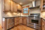 This charming kitchen features beautiful light wood cabinetry and sleek stainless steel appliances, including a modern gas range and a double-drawer dishwasher.