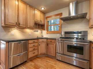 This charming kitchen features beautiful light wood cabinetry and sleek stainless steel appliances, including a modern gas range and a double-drawer dishwasher.