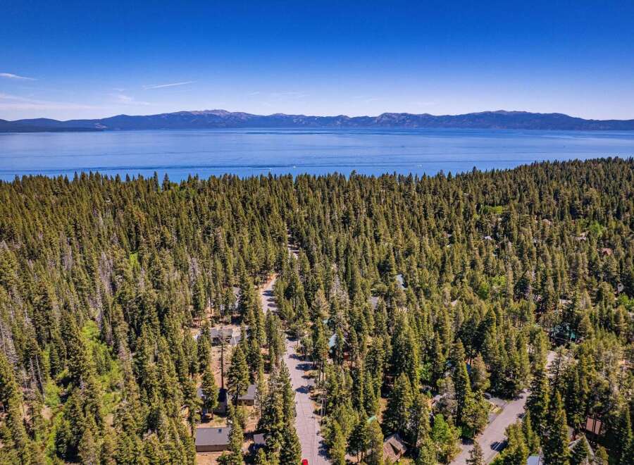 Discover your dream mountain retreat nestled amidst a dense forest with stunning views of a vast, blue lake and distant mountains.