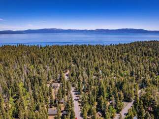 Discover your dream mountain retreat nestled amidst a dense forest with stunning views of a vast, blue lake and distant mountains.