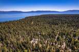 Discover your dream home nestled within a serene pine forest, offering breathtaking views of a vast blue lake and distant mountains.