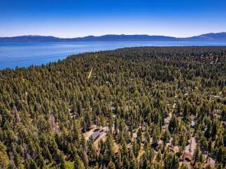 Discover your dream home nestled within a serene pine forest, offering breathtaking views of a vast blue lake and distant mountains.