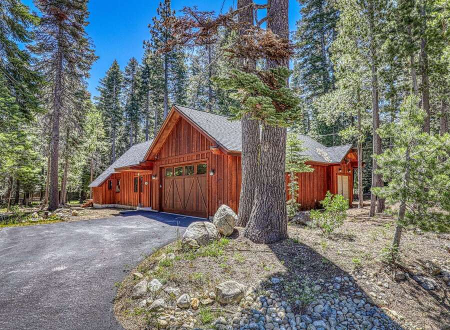 Nestled amongst tall pine trees, this charming wooden home features a rustic aesthetic with a prominent garage door and warm wood siding.