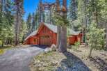 Nestled amongst tall pine trees, this charming wooden home features a rustic aesthetic with a prominent garage door and warm wood siding.