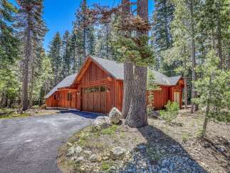 Nestled amongst tall pine trees, this charming wooden home features a rustic aesthetic with a prominent garage door and warm wood siding.