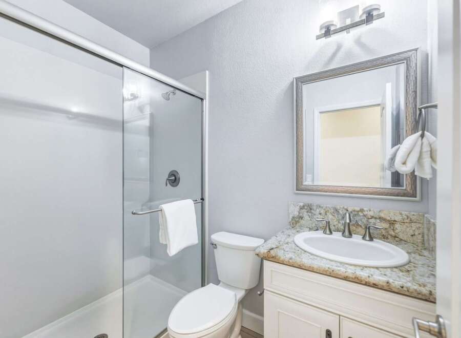 This modern bathroom features a sleek glass-enclosed shower and a stylish vanity with a granite countertop.