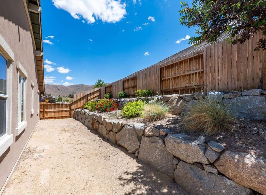 Discover a beautifully landscaped backyard featuring a tiered stone retaining wall adorned with vibrant red flowers and lush greenery.