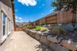 Discover a beautifully landscaped backyard featuring a tiered stone retaining wall adorned with vibrant red flowers and lush greenery.