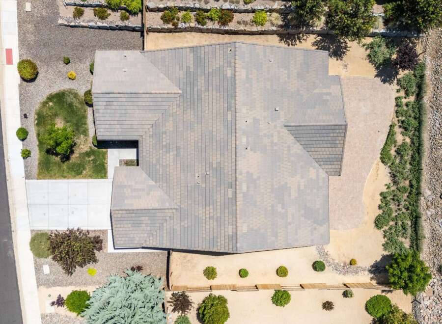 Discover this stunning aerial view of a modern home featuring a multi-faceted roof design and a spacious paved driveway.