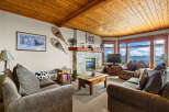 Experience breathtaking mountain views from this cozy living room, featuring a stone fireplace and a warm, wood-paneled ceiling.