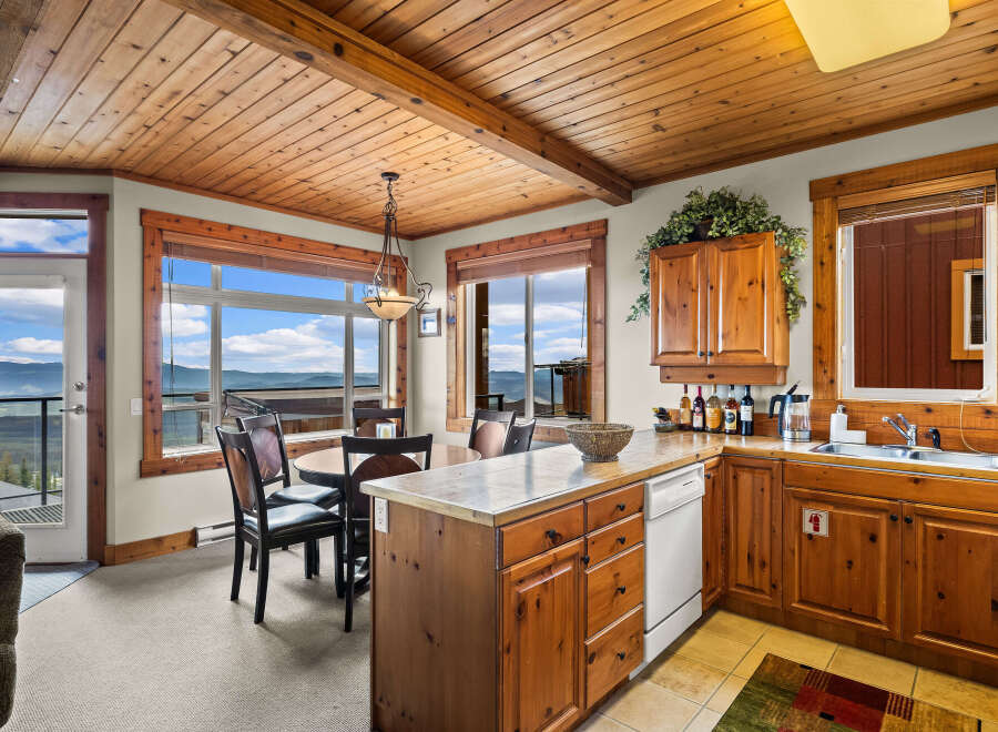 Experience breathtaking mountain views from this charming dining and kitchen area, featuring a cozy round dining table and a well-equipped kitchen with ample wooden cabinetry.