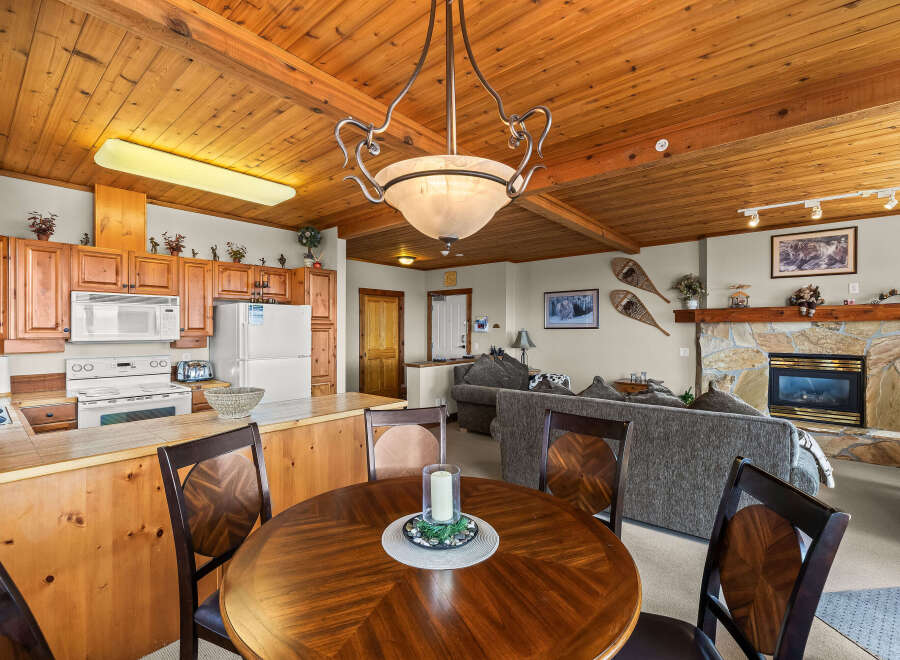 Experience cozy living in this charming mountain retreat, featuring a warm wood-paneled ceiling and a rustic stone fireplace.