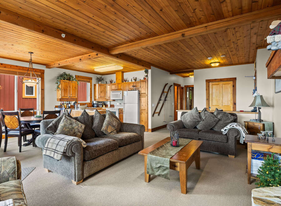 Experience cozy mountain living in this charming living and dining area, featuring a warm wood-paneled ceiling and exposed beams.
