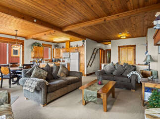 Experience cozy mountain living in this charming living and dining area, featuring a warm wood-paneled ceiling and exposed beams.