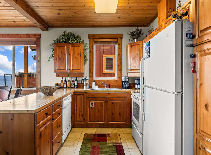 This charming kitchen features warm wooden cabinetry and countertops, complemented by a spacious window offering stunning mountain and sky views.