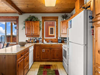 This charming kitchen features warm wooden cabinetry and countertops, complemented by a spacious window offering stunning mountain and sky views.