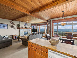 Experience breathtaking mountain views from this stunning living and dining area, featuring a cozy stone fireplace and a warm, wood-paneled ceiling.