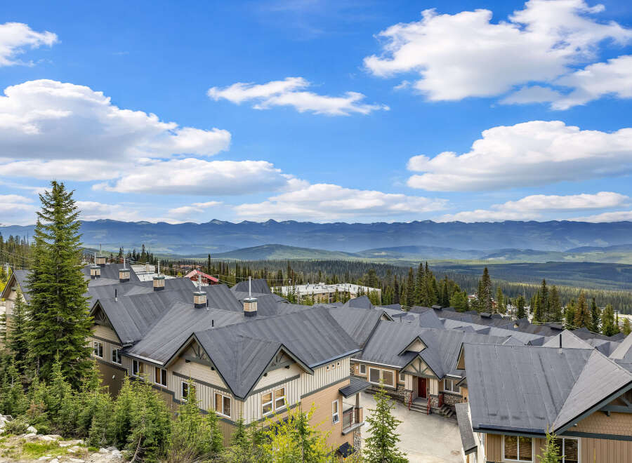 Discover this stunning mountain property featuring a row of charming townhomes with dark pitched roofs, nestled amidst lush evergreen trees.