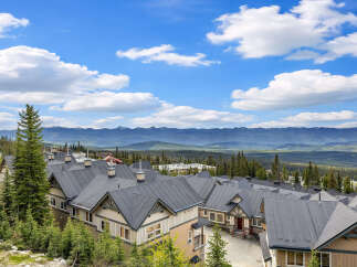Discover this stunning mountain property featuring a row of charming townhomes with dark pitched roofs, nestled amidst lush evergreen trees.