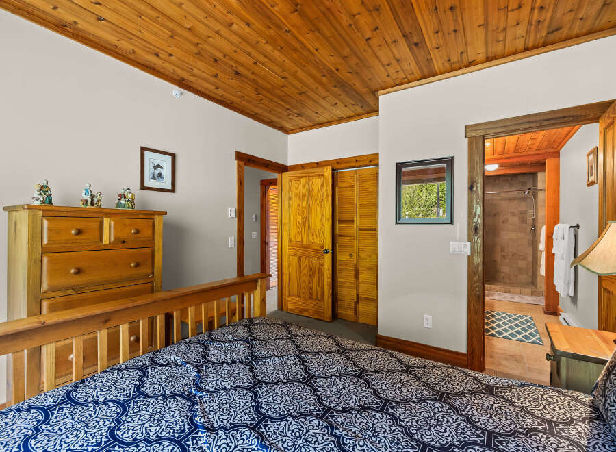 Experience rustic charm in this cozy bedroom featuring a wooden plank ceiling and a comfortable bed with a striking blue and white patterned comforter.
