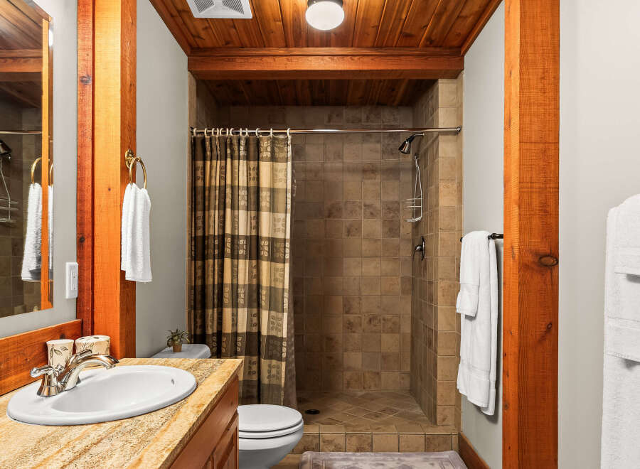 Experience rustic charm in this bathroom featuring a tiled walk-in shower with a patterned shower curtain and a wooden beam accent.