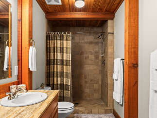 Experience rustic charm in this bathroom featuring a tiled walk-in shower with a patterned shower curtain and a wooden beam accent.
