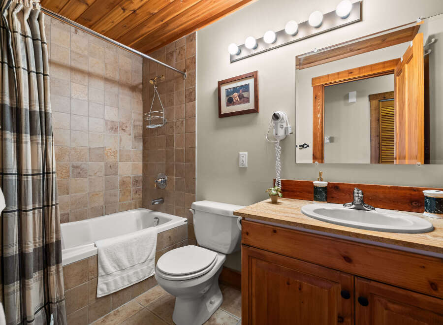 This charming bathroom features a tiled shower/tub combo with a plaid shower curtain, a white toilet, and a wooden vanity with a granite countertop.