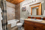 This charming bathroom features a tiled shower/tub combo with a plaid shower curtain, a white toilet, and a wooden vanity with a granite countertop.