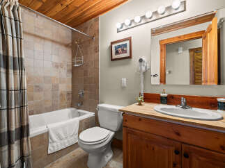 This charming bathroom features a tiled shower/tub combo with a plaid shower curtain, a white toilet, and a wooden vanity with a granite countertop.