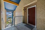 Experience mountain living with this charming condo's exterior entrance, featuring a striking red door and a scenic balcony overlooking a wooded landscape.