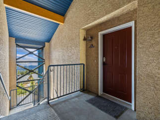 Experience mountain living with this charming condo's exterior entrance, featuring a striking red door and a scenic balcony overlooking a wooded landscape.