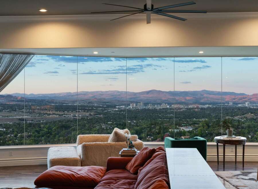 Experience breathtaking panoramic views from this stunning living room, featuring expansive floor-to-ceiling windows that showcase a sprawling cityscape and majestic mountain range.