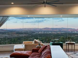 Experience breathtaking panoramic views from this stunning living room, featuring expansive floor-to-ceiling windows that showcase a sprawling cityscape and majestic mountain range.