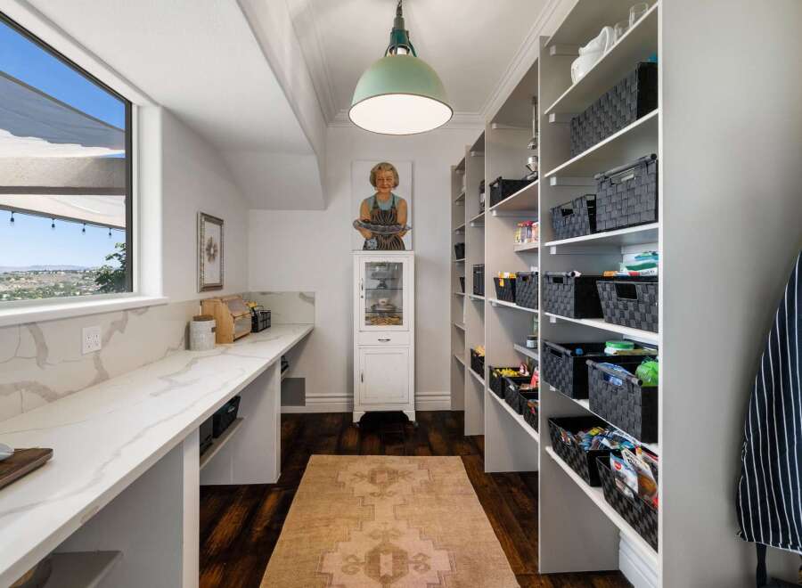 Discover ample storage in this spacious pantry, featuring floor-to-ceiling shelving equipped with convenient black woven baskets.