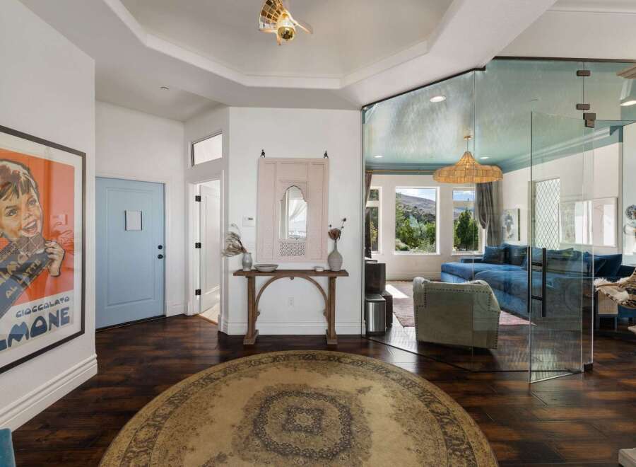 Step into this stunning entryway featuring a bold vintage poster and a light blue door, leading to a living area with breathtaking mountain views through expansive glass walls.