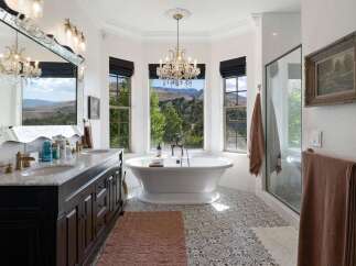 Indulge in luxury with this stunning bathroom featuring a freestanding soaking tub positioned perfectly to enjoy breathtaking mountain views through large bay windows.