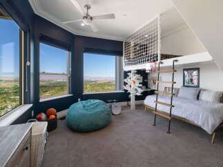 Experience breathtaking panoramic views from this stunning bedroom, featuring expansive windows that showcase a vibrant cityscape and rolling hills.