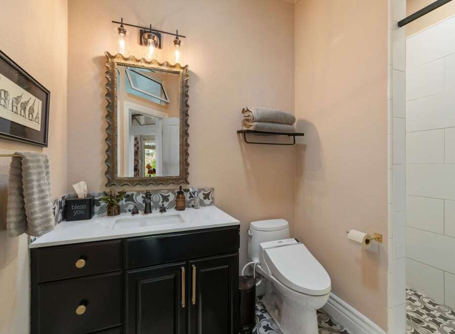 This charming bathroom features a modern black vanity with gold hardware, complemented by a decorative tiled backsplash.