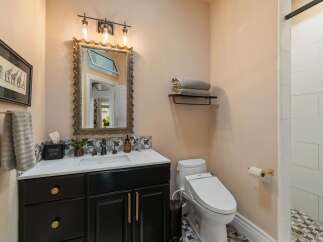 This charming bathroom features a modern black vanity with gold hardware, complemented by a decorative tiled backsplash.