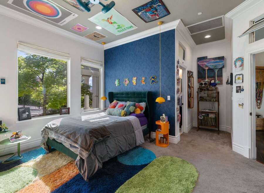 This vibrant bedroom features a plush green velvet headboard and a large window offering serene views of lush greenery.