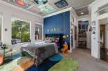 This vibrant bedroom features a plush green velvet headboard and a large window offering serene views of lush greenery.